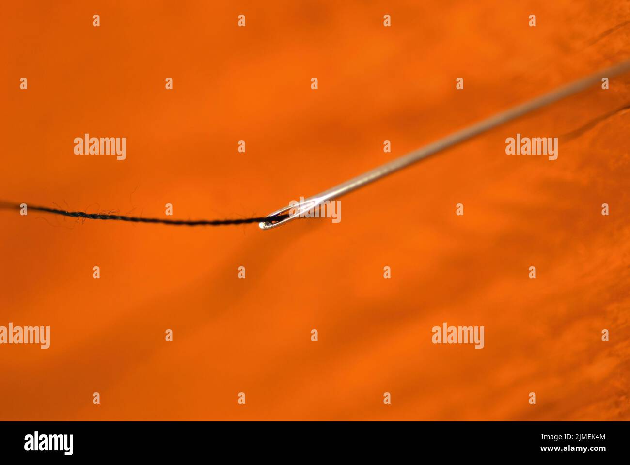 Selektiver Fokus, Nadel mit Nähgarn einfädeln, Nähkonzept, selektiver Fokus auf das Knopfloch mit dem Faden, unfokussierter Hintergrund Stockfoto