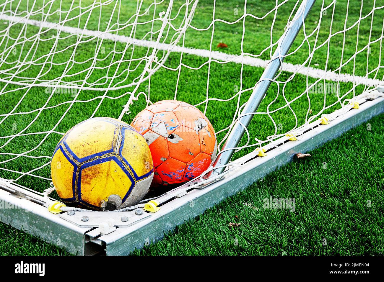Zwei zerlumpte, schäbige Fußballbälle in der Ecke des Fußball-Tornetzes Stockfoto