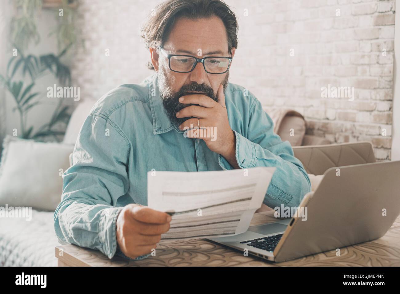 Ein Mann zu Hause las besorgt einen Strom oder Kosten Rechnung vor einem Laptop. Menschen zu Hause mit wirtschaftlichen Problemen. Online-Zahlung Hauskosten. Eins Stockfoto