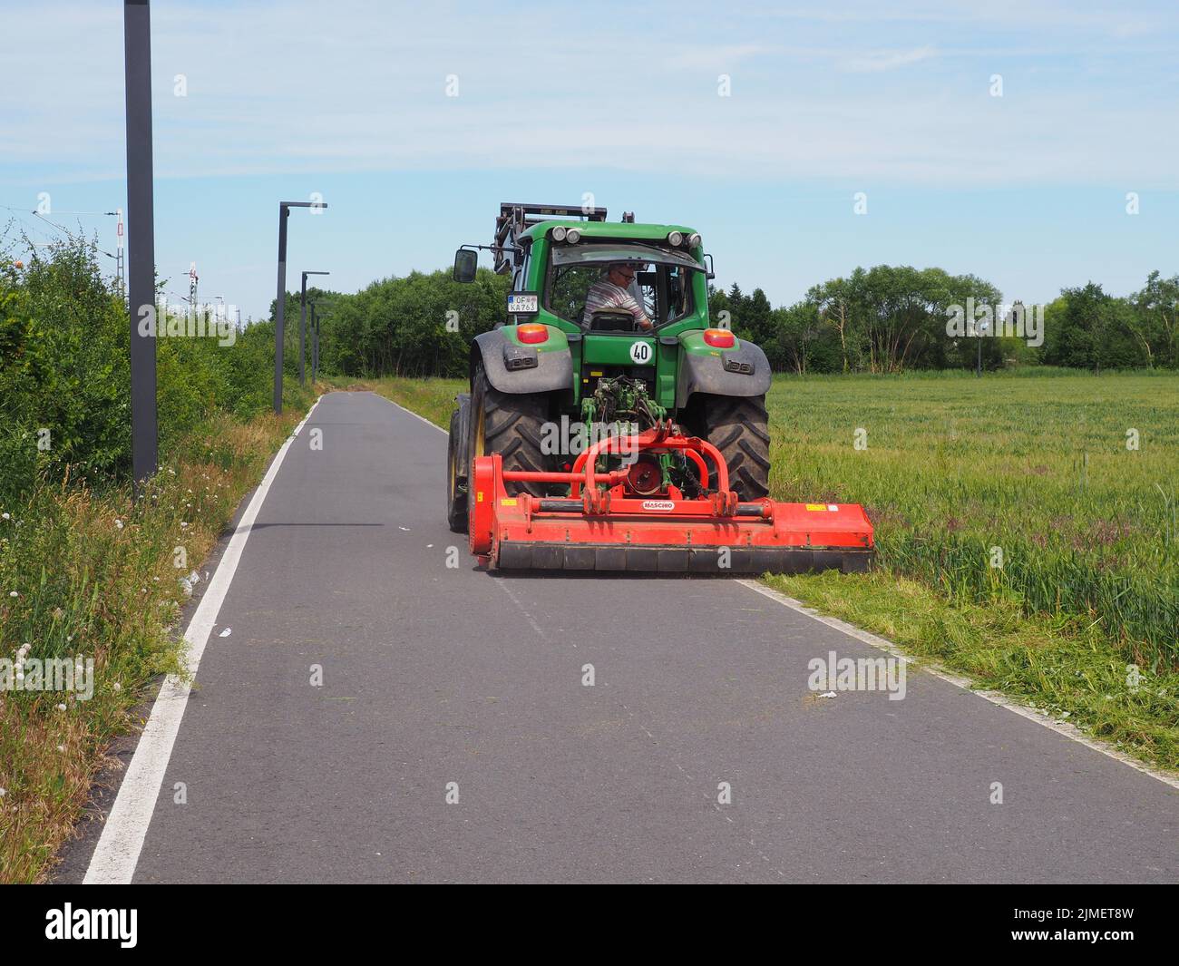 Ein roter Traktor mäht eine Graswiese am Rande einer Radstraße in Egelsbach, Deutschland Stockfoto