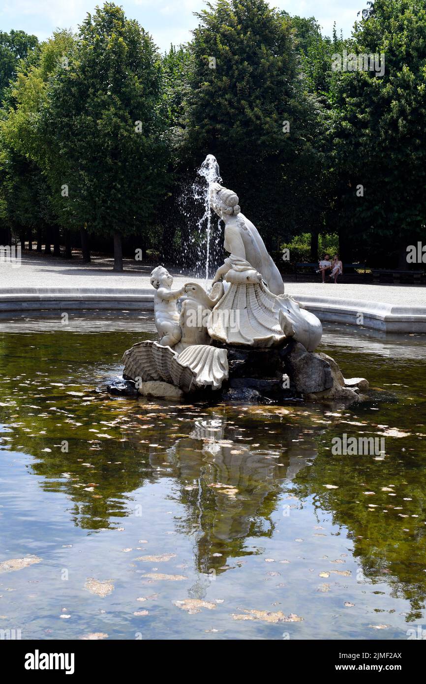 Wien, Österreich - 01. August 2022: Nicht identifizierte Menschen ruhen auf einer Bank am westlichen Najadenbrunnen in einem Rondeau entlang der baumgesäumten Alleen im Park o Stockfoto