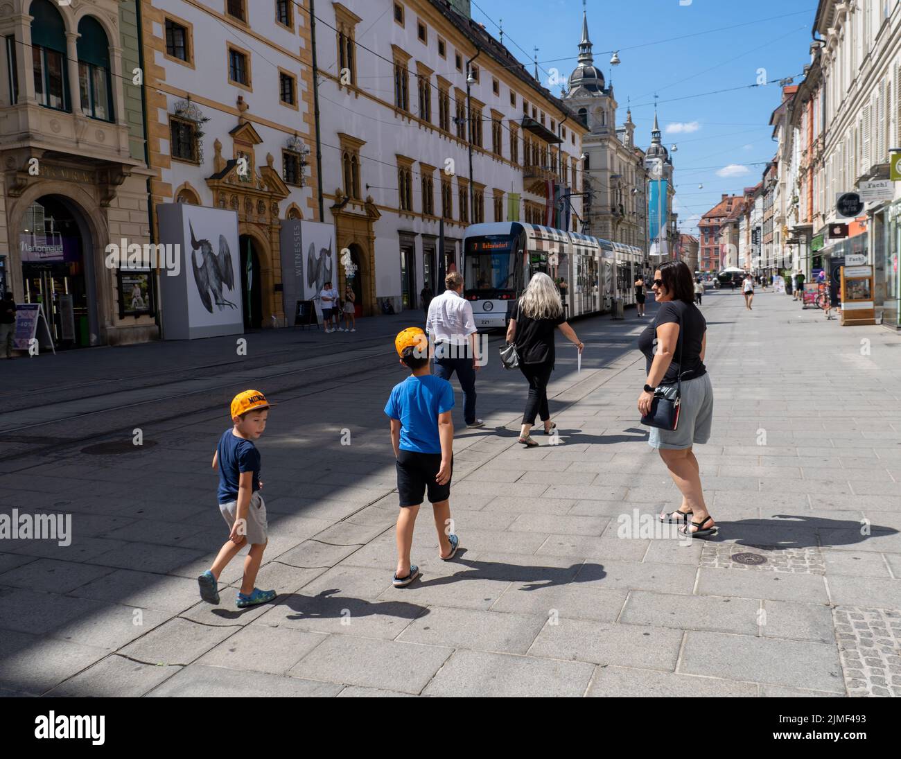 Eine Frau und zwei Kinder gehen auf einer Straße mit Geschäften und Restaurants im Stadtzentrum. Graz, Österreich Stockfoto