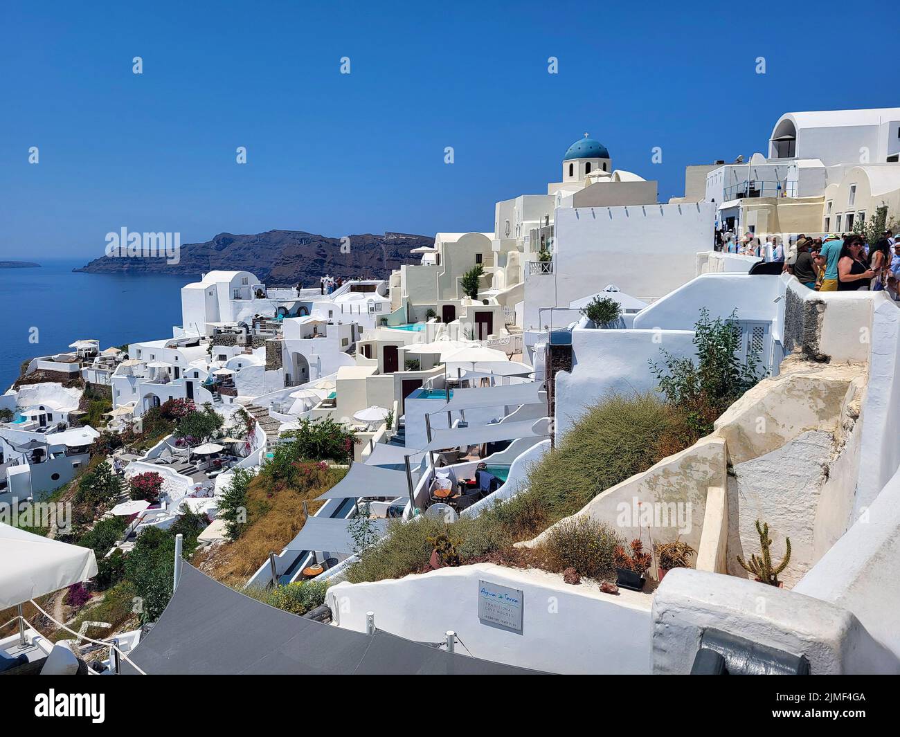 Oia, Griechenland - 22. Juni 2022: Nicht identifizierte Menschen in einer engen Straße und schöner Blick über die Stadt auf der Insel Santorini Stockfoto