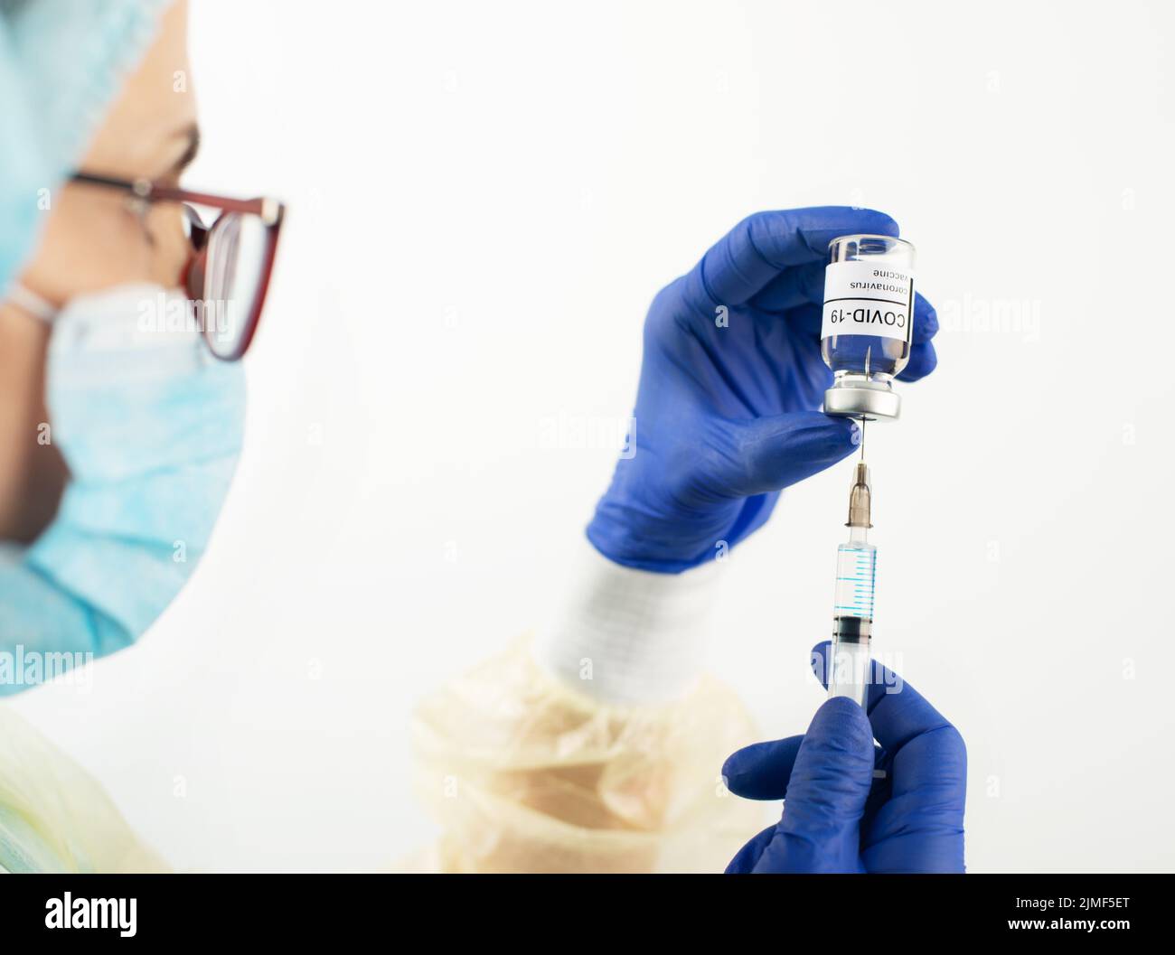Kaukasische Ärztin mittleren Alters mit Schutzbrille und Handschuhen, die eine Spritze für die Injektion des Coronavirus-Impfstoffs vorbereitet Stockfoto