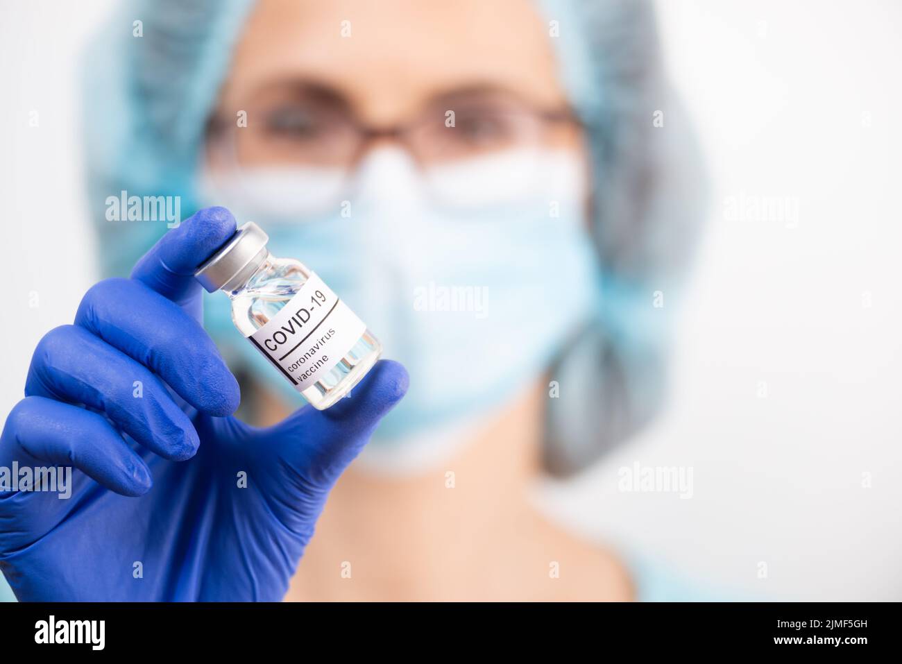 Ärztin mittleren Alters in Schutzbrille und Handschuhen hält Flasche mit Coronavirus-Impfstoff Stockfoto