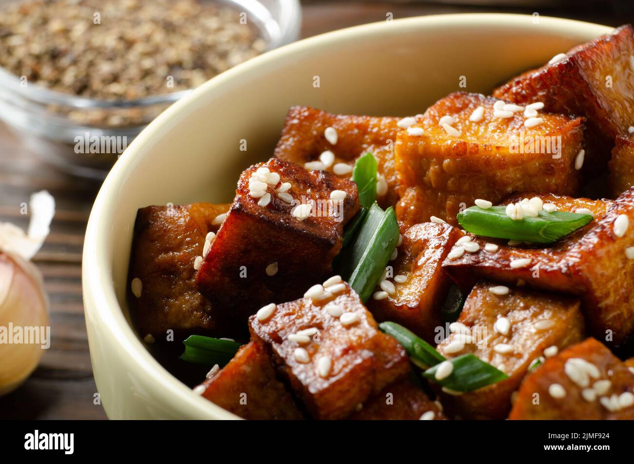 Nahaufnahme von knusprig gebratenen Tofu-Stücken mit Schnittlauch und Sesam in Tonschale Stockfoto