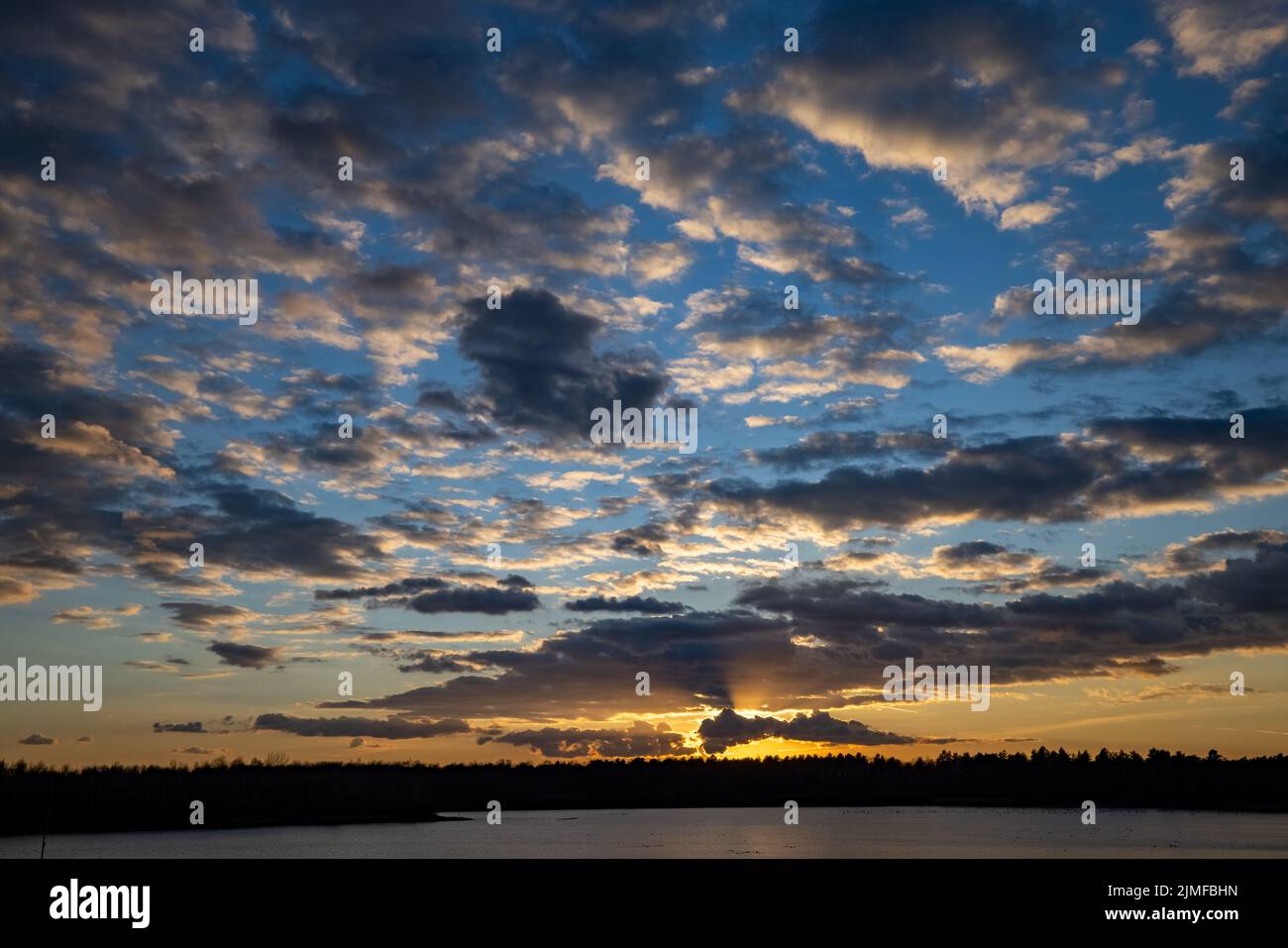 Epische rote, blaue und goldene Wolken über dem Waldsee bei Sonnenaufgang. Dramatische, farbenfrohe Wolkenlandschaft. Symmetriereflexionen auf dem Wat Stockfoto