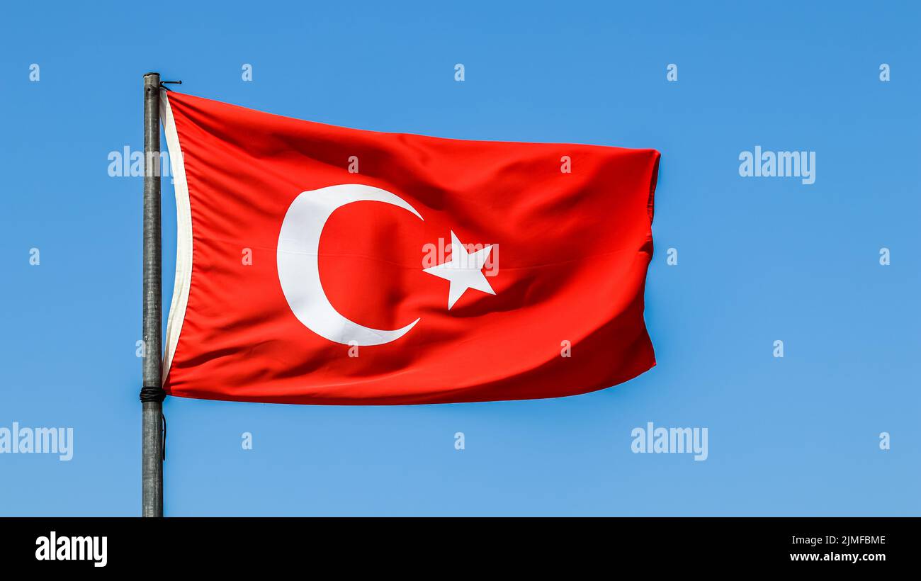 Nationalflagge der Türkei auf einem Fahnenmast im Wind auf einem Hintergrund von blauem Himmel. Stockfoto