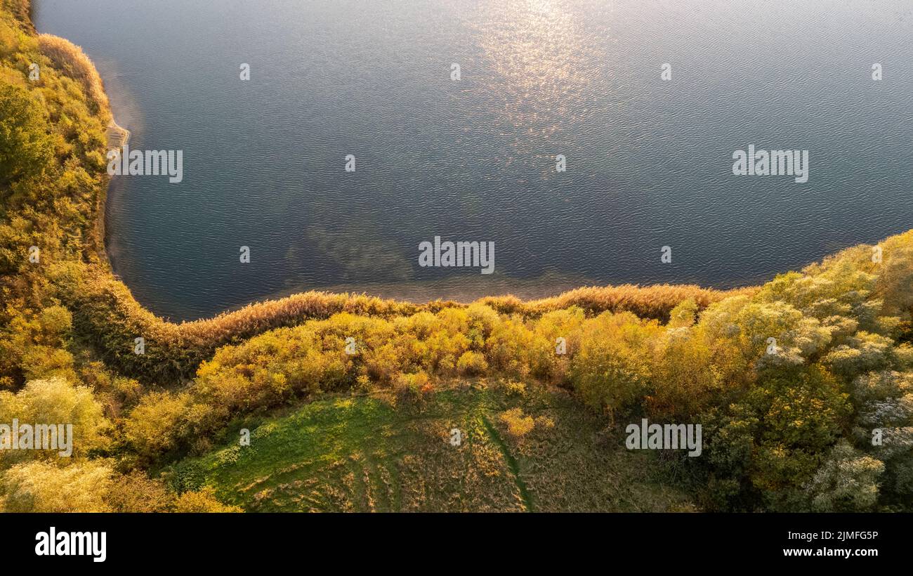 Luftaufnahme eines malerischen Ortes, an dem im Frühling das durchsichtige türkisfarbene Wasser eines Waldsees auf ein steineres Ufer mit Bäumen trifft. Stockfoto