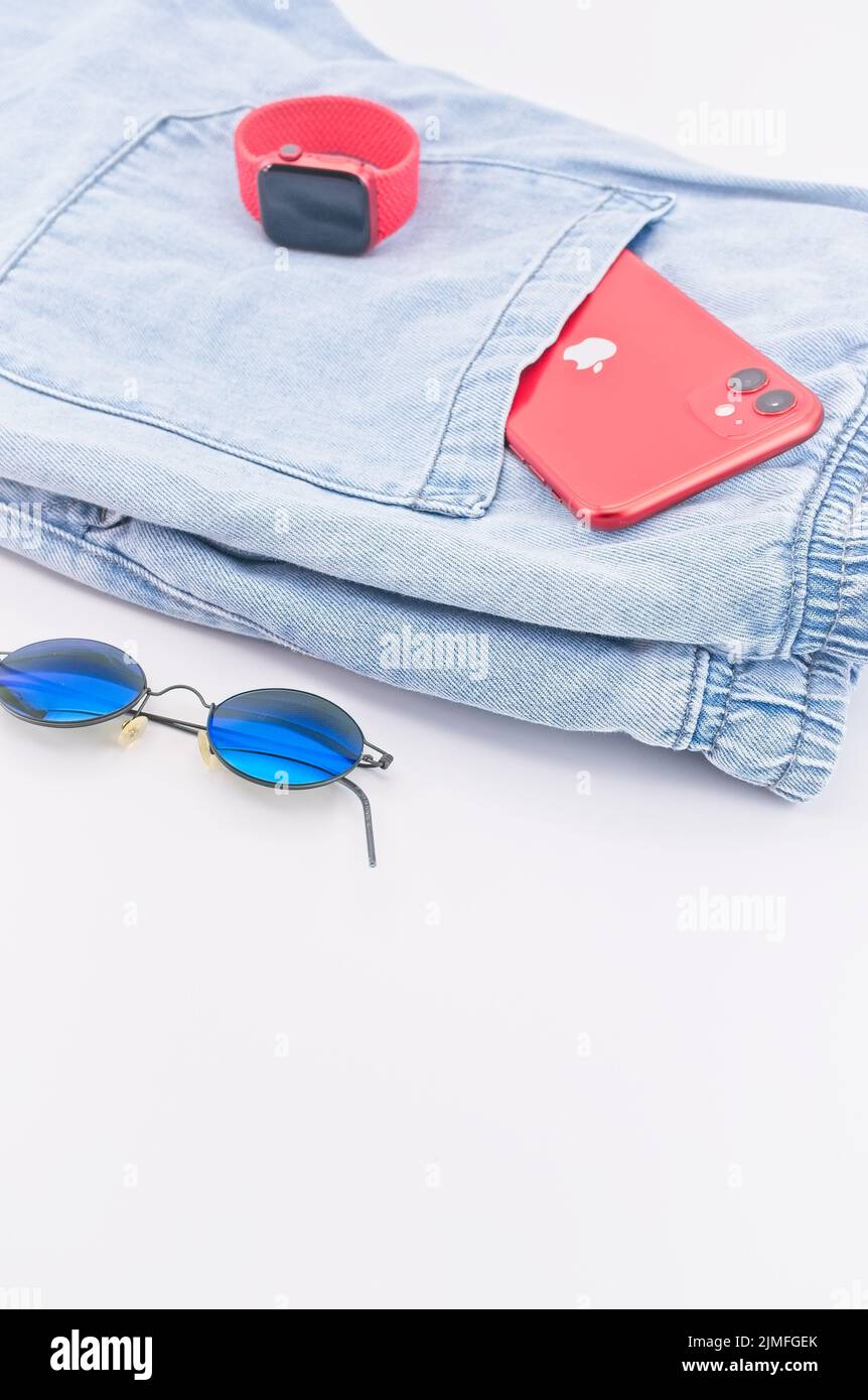 IPhone der Marke Apple, Apple-Uhr und Sonnenbrille sowie legere Kleidung auf dem Schreibtisch Stockfoto