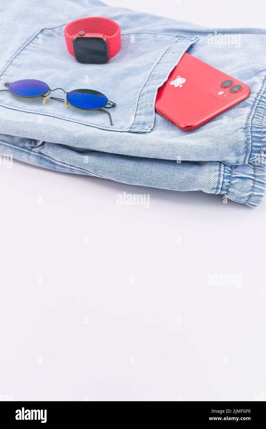 IPhone der Marke Apple, Apple-Uhr und Sonnenbrille sowie legere Kleidung auf dem Schreibtisch Stockfoto