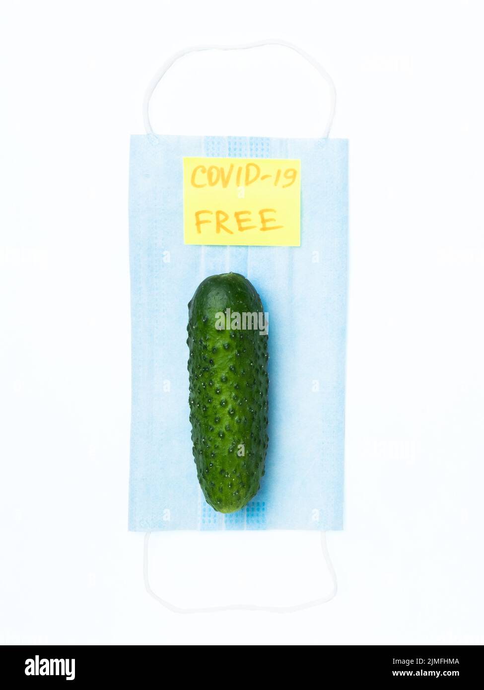 Flach liegend. Grüne Gurke auf einer blauen medizinischen Maske. Isoliert. COVID-19 KOSTENLOS. Stockfoto