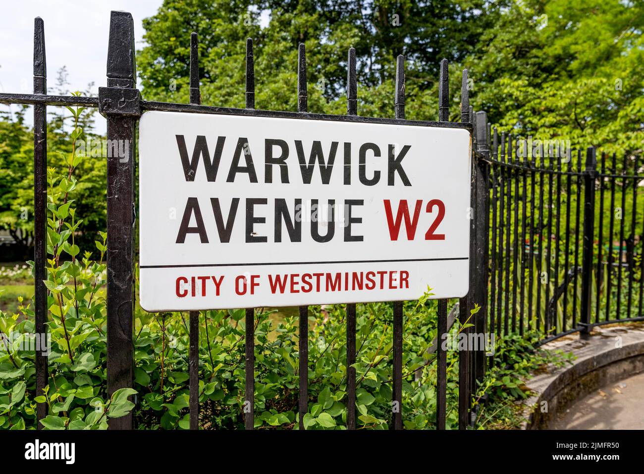 Metall- und weißes Straßenschild auf einem Zaun, der auf die Warwick Avenue zeigt, in London, City of Westminster, England, Vereinigtes Königreich Stockfoto