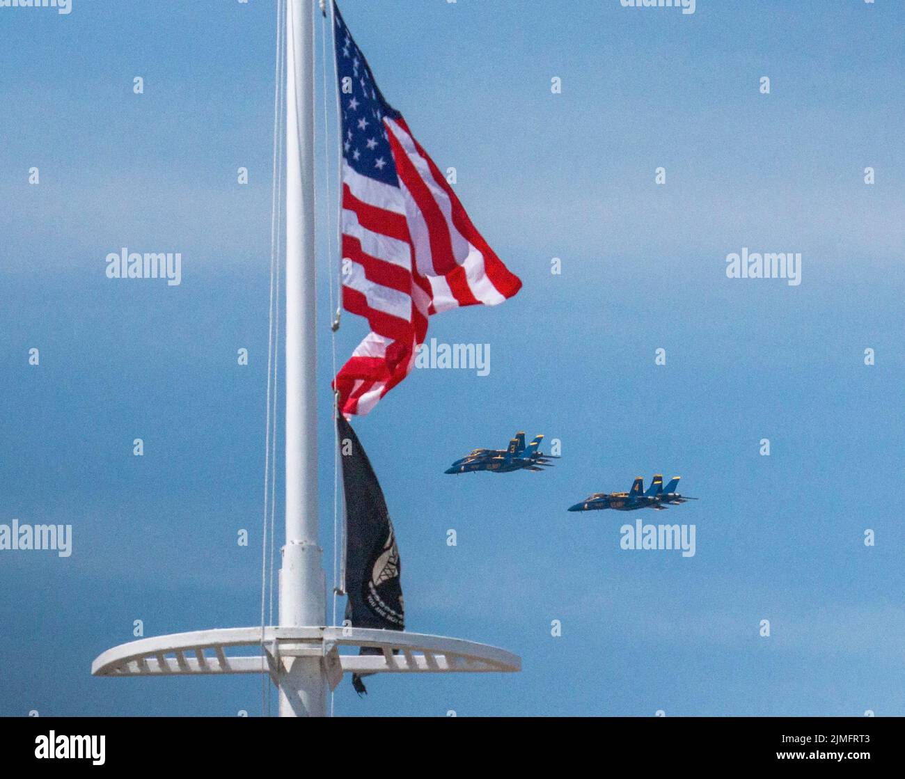 Die Blue Angels der US Navy fliegen in Formation hinter einer amerikanischen Flagge, die während einer Airshow im Wind weht. Stockfoto