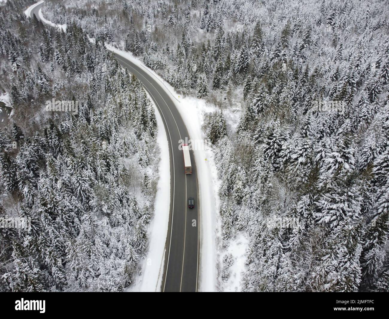 Kurvige Straße durch den Wald im Winter. Asphalt durch den Pass auf die Spitze des Berges in Rumänien. Stockfoto