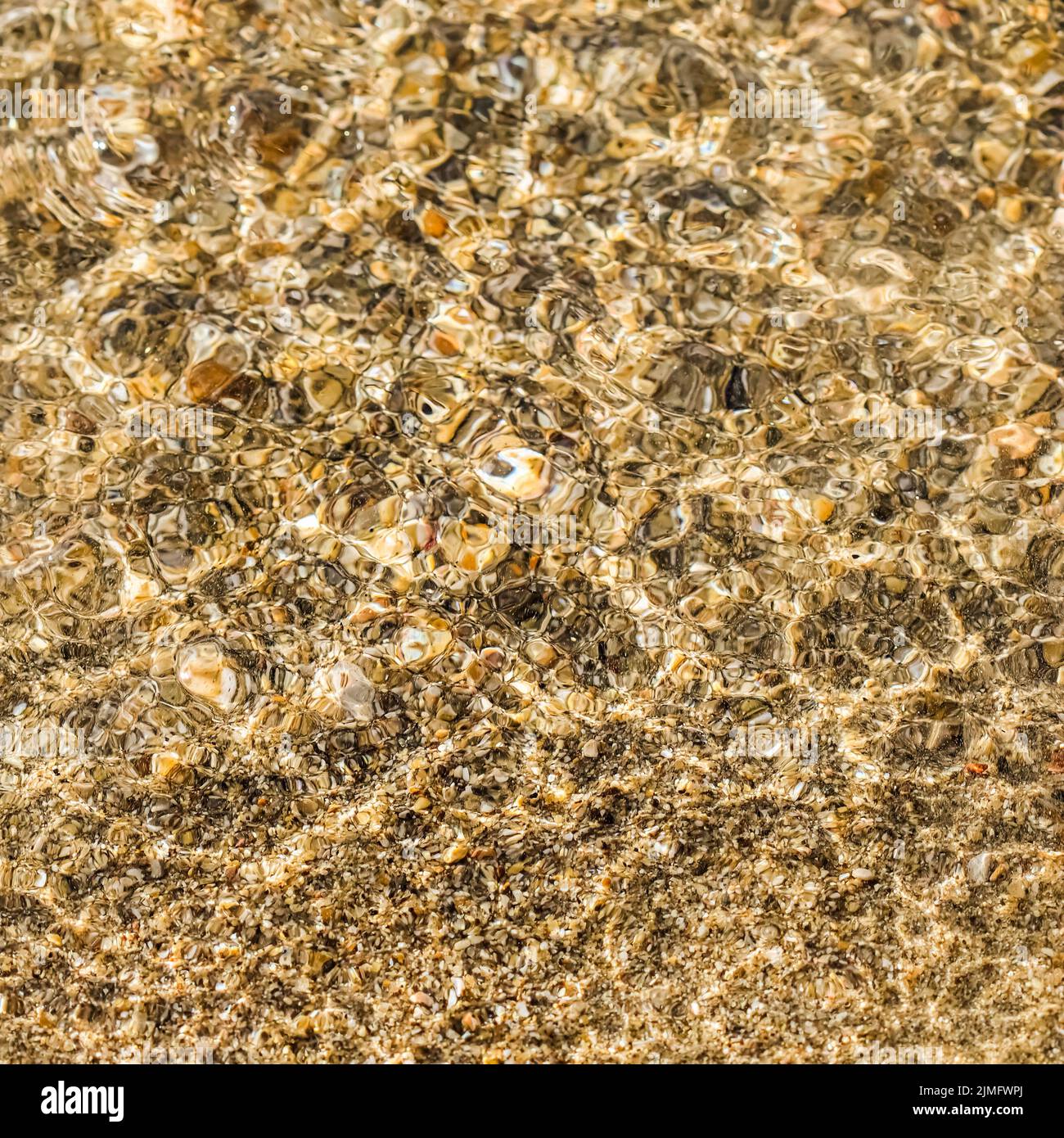 Ein Hintergrund aus Sand, kleinen Kieselsteinen und fließenden Wellen am Meeresstrand. Konzept für Sommerferien Stockfoto