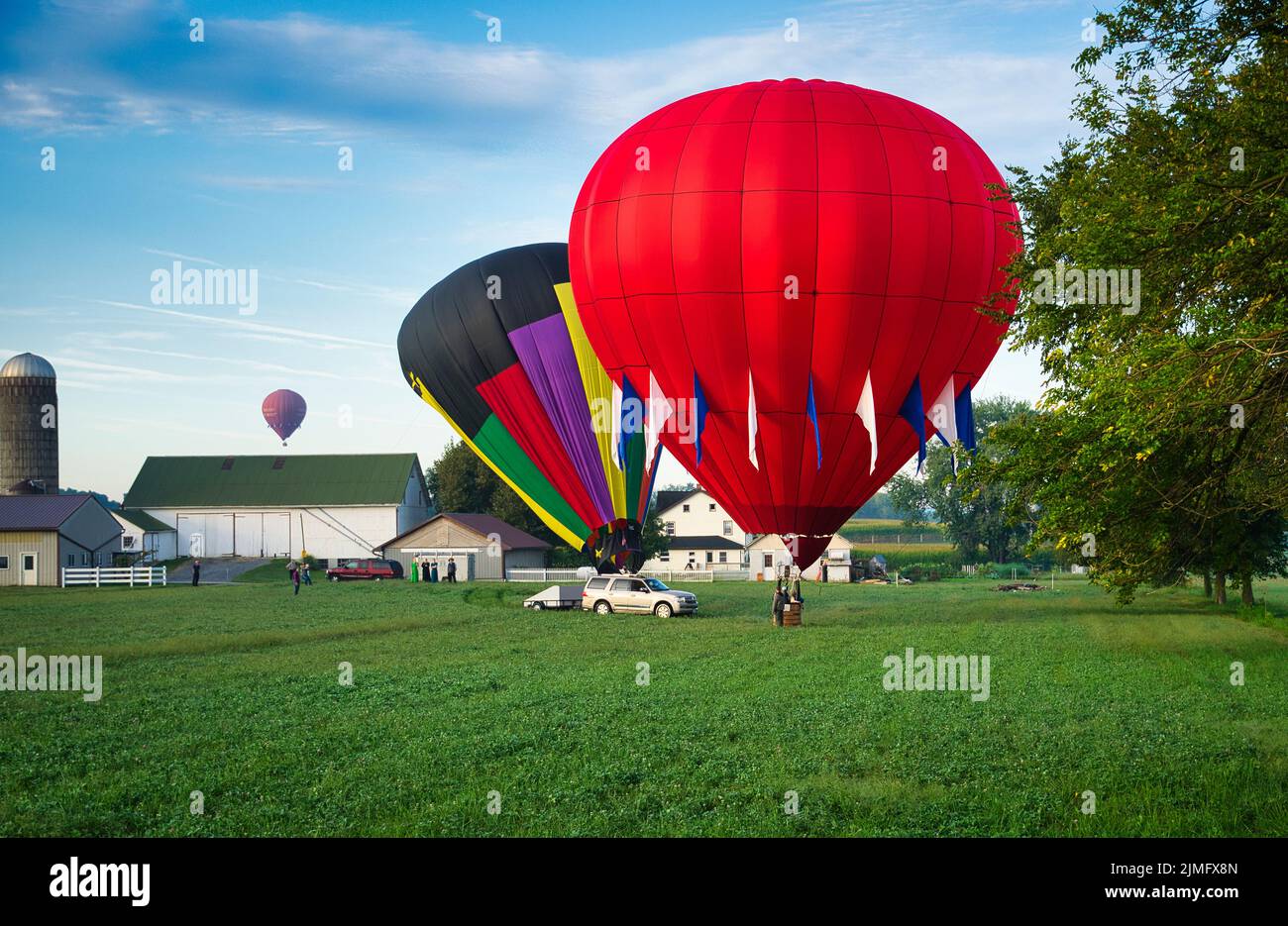 Mehrere Heißluftballons landen auf Ackerland, während die Amish auf sie schauen Stockfoto