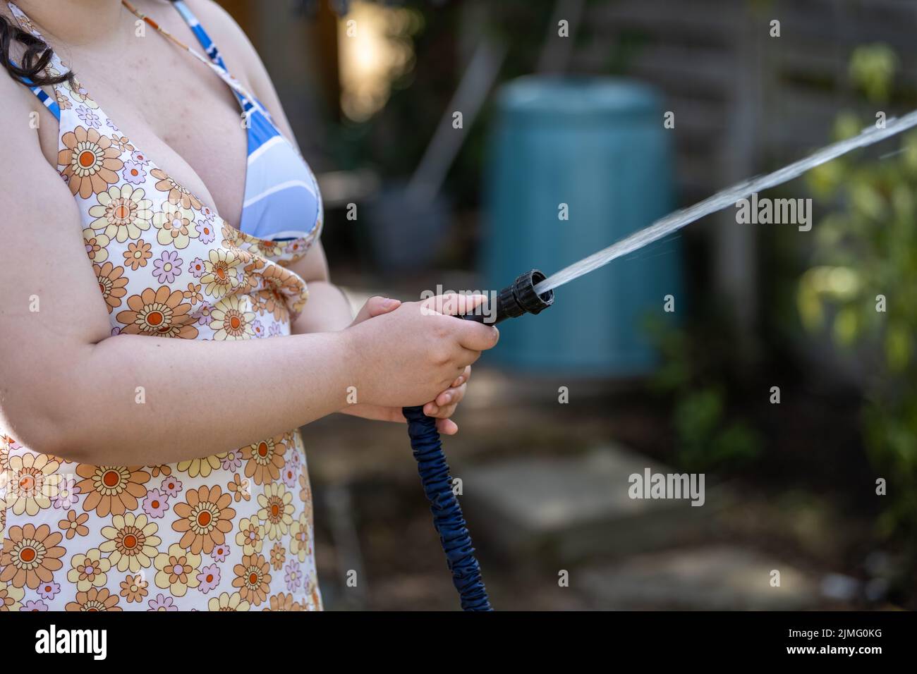 Junge Frau bewässert den Garten mit einer Schlauchleitung, bevor das Rohrleitungsverbot aufgrund von Dürre, Wasserknappheit und schlechten Niederschlägen in Kraft tritt. Stockfoto