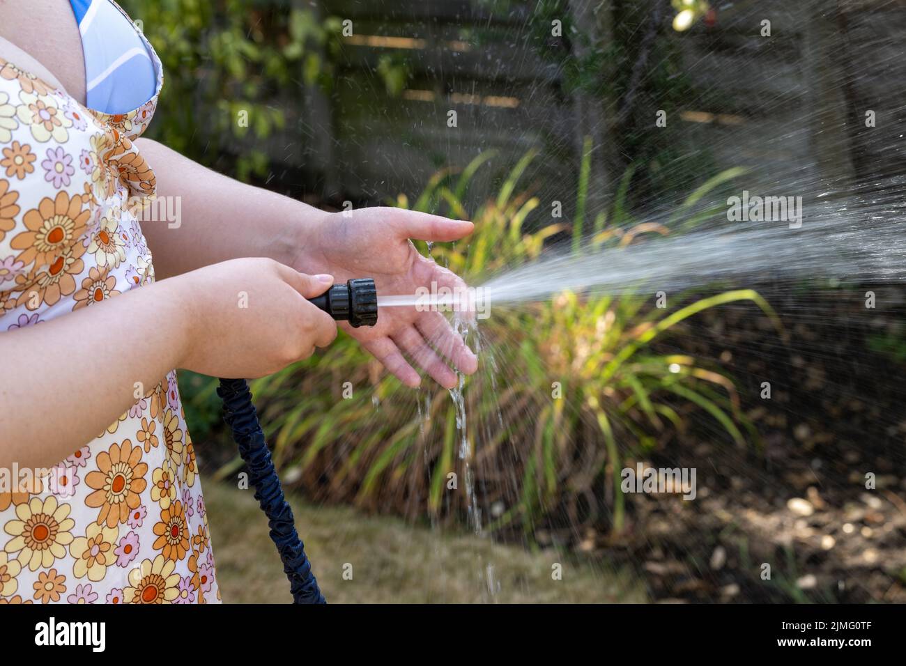 Junge Frau bewässert den Garten mit einer Schlauchleitung, bevor das Rohrleitungsverbot aufgrund von Dürre, Wasserknappheit und schlechten Niederschlägen in Kraft tritt. Stockfoto