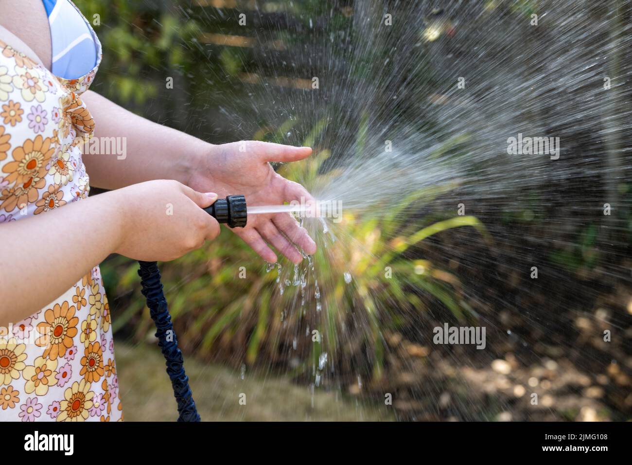 Junge Frau bewässert den Garten mit einer Schlauchleitung, bevor das Rohrleitungsverbot aufgrund von Dürre, Wasserknappheit und schlechten Niederschlägen in Kraft tritt. Stockfoto