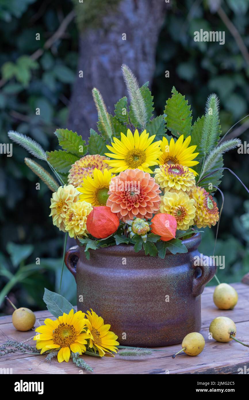 Bouquet von orangefarbenen und gelben Dahlien und Sonnenblumen in altem Tontopf Stockfoto