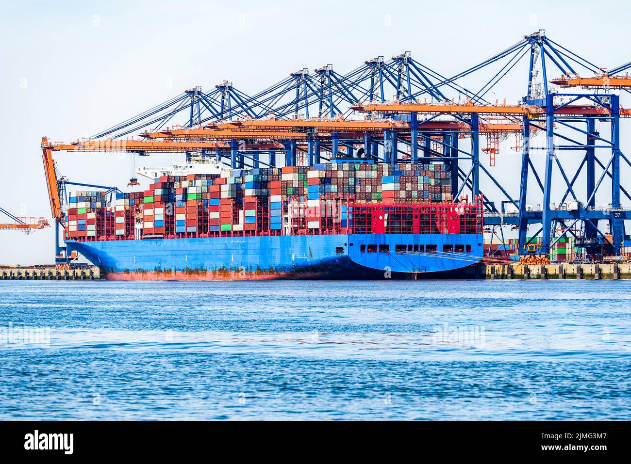 Große Containerschiffe werden an einem klaren Sommertag beladen, während sie an ein kommerzielles Dock mit hohen Portalkranen gebunden werden Stockfoto