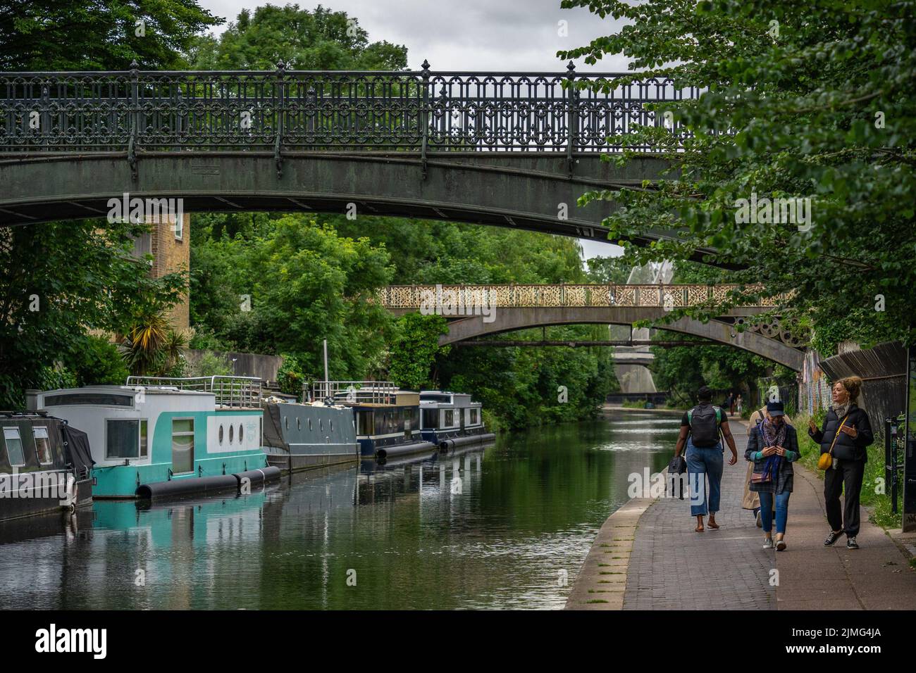 London, Großbritannien - 09 2022. Juni: Menschen, die auf dem Bürgersteig des Regent-Kanals spazieren, während Schmalbboote auf dem Wasser schweben; Londoner Alltag Stockfoto