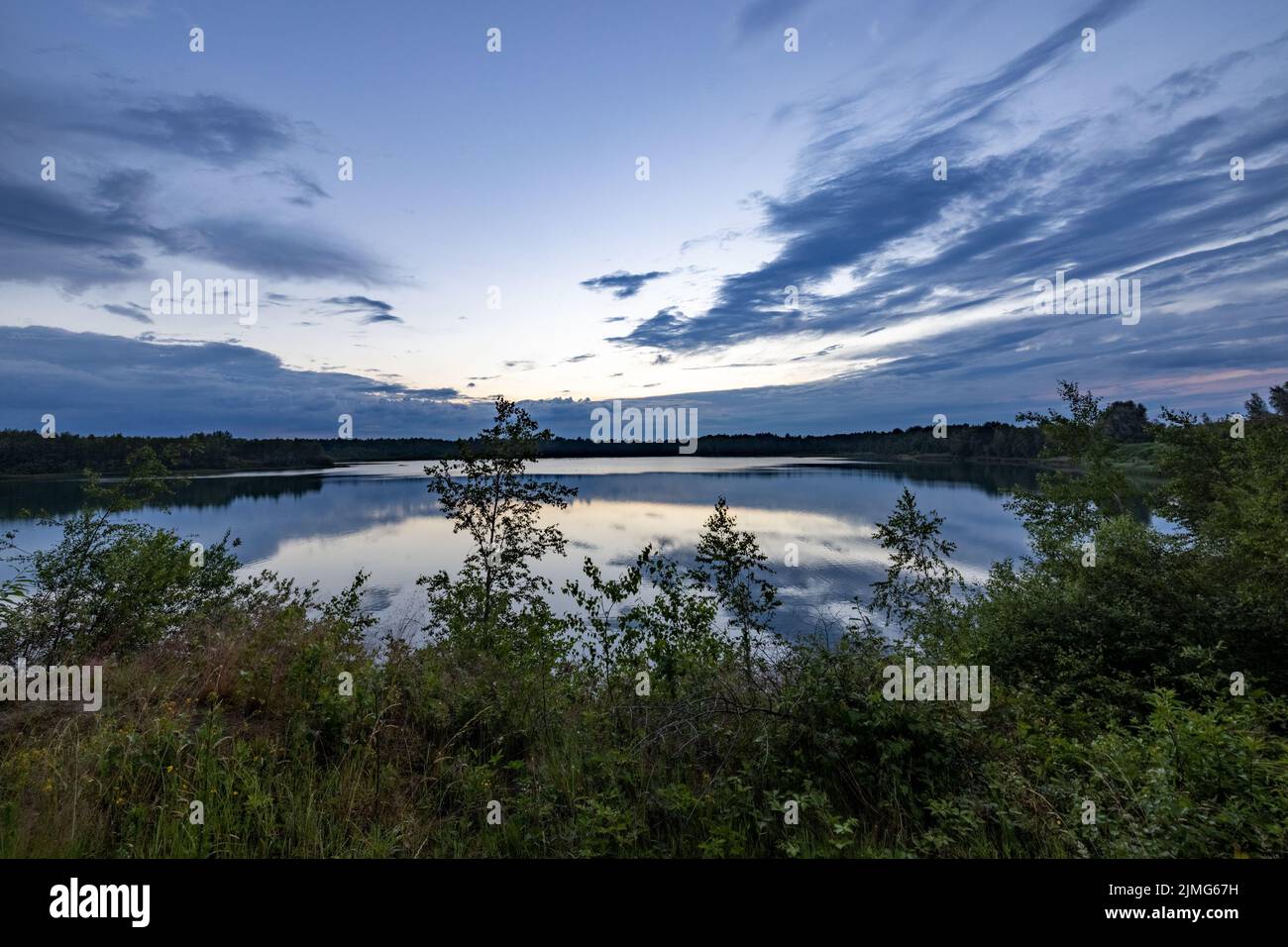 Ein wunderschöner blauer See mit grünem Baum im Vordergrund unter einem dramatischen blauen Abendhimmel Stockfoto