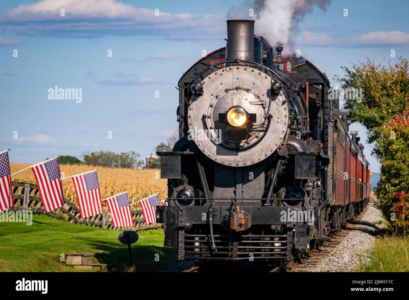 Antike Dampflok nähert sich durch Maisfelder mit American Flags Lining the Track Stockfoto