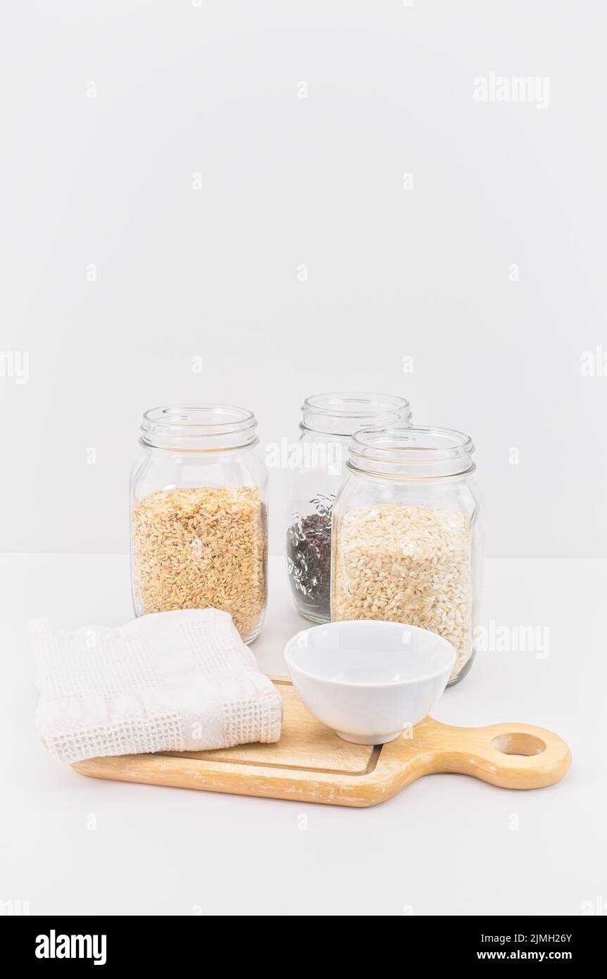 Glas und Behälter mit Bio-Reis auf einem weißen Tisch und Hintergrund Stockfoto