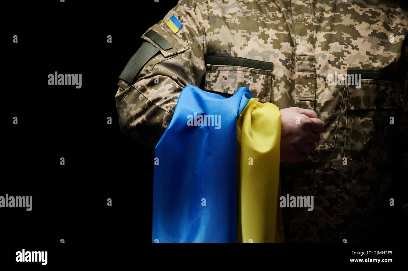 Ukrainischer Soldat hält die Flagge des unabhängigen Staates Ukraine. Standhaftigkeit und Mut der Menschen im Kampf gegen Stockfoto