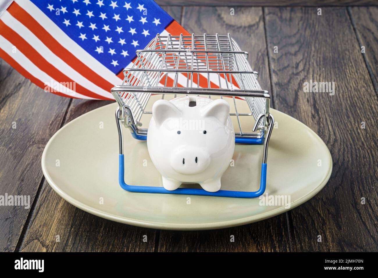 Sparschwein auf Teller unter dem Warenkorb und USA Flagge. Konzept der Handelsinflation Stockfoto