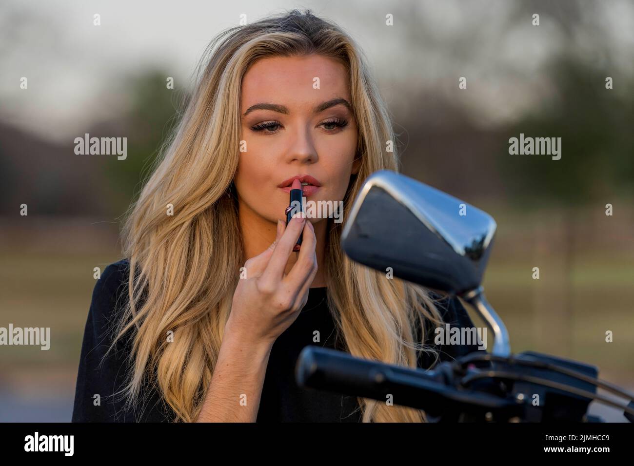 Ein schönes blondes Model genießt das Wetter im Freien, während sie mit ihrem Motorrad posiert Stockfoto