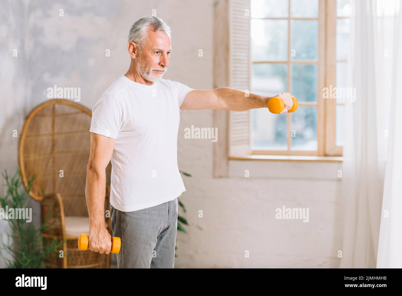 Fit Senior Mann Training mit orangen Hanteln nach Hause Stockfoto