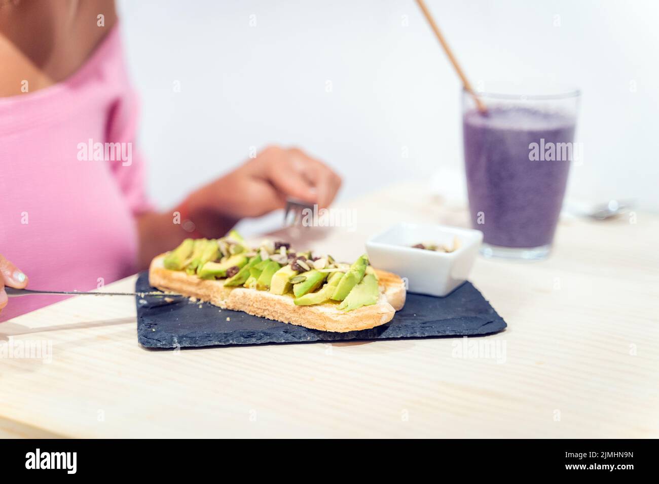 Nahaufnahme einer Frau, die beim Frühstück einen Avocado-Toast isst und Smoothie trinkt. Gesundes Lebensmittelkonzept. Stockfoto