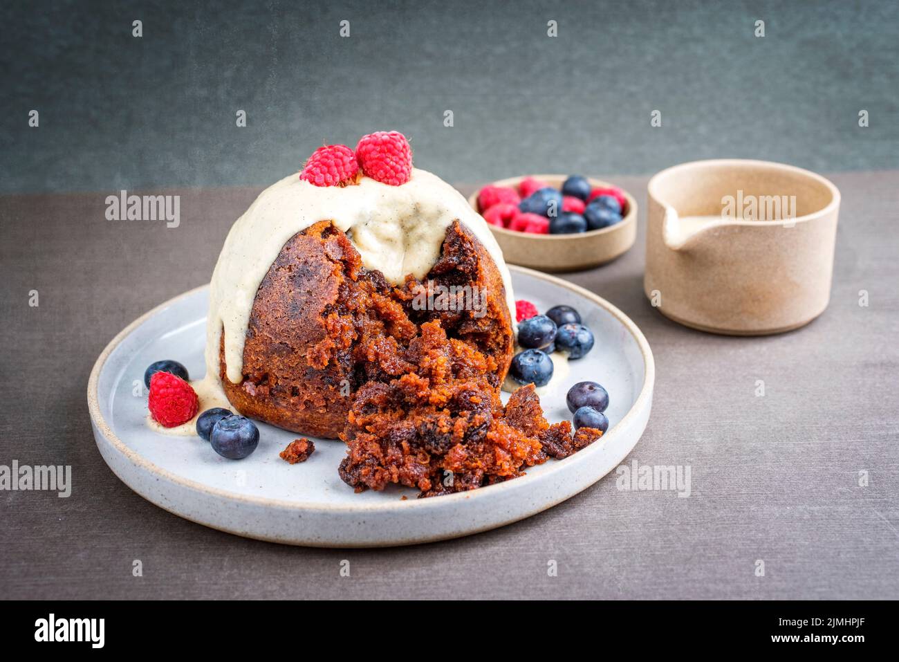 Traditioneller australischer Pflaumenpudding als Nahaufnahme mit Früchten und Vanille-Rum-Sauce auf einem Dessertteller im modernen Design mit Copy-SPAC Stockfoto