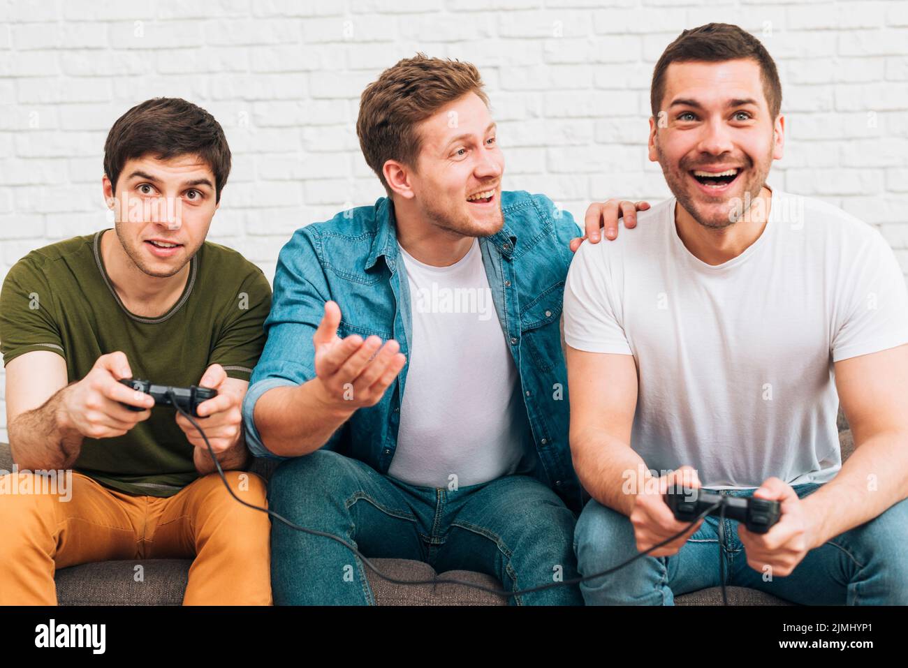 Drei männliche Freunde sitzen zusammen und genießen Videospiele Stockfoto