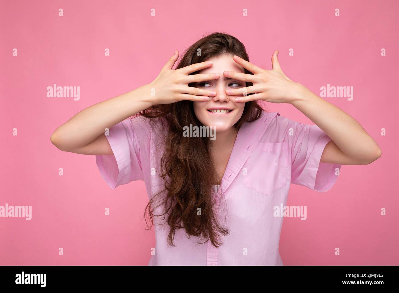 Porträt von jungen emotionalen positiv lustig schöne lockige Brünette Frau mit aufrichtigen Emotionen tragen lässig rosa Hemd Isolat Stockfoto