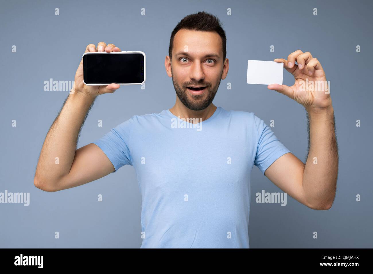 Foto eines hübschen jungen unrasierten Brunet-Mannes mit Bart, der täglich ein blaues T-Shirt auf blauem Hintergrund trägt, das isoliert und U hält Stockfoto