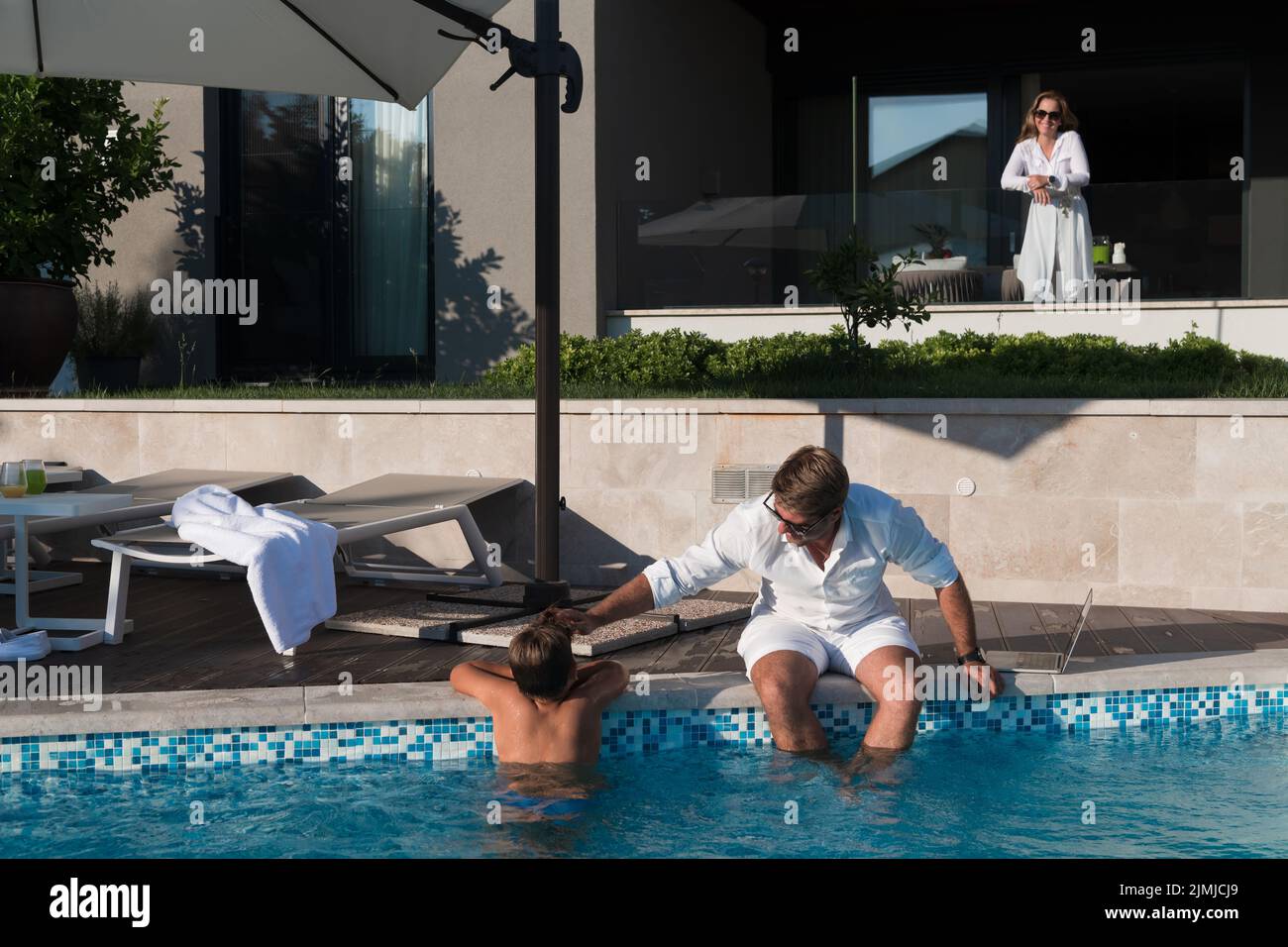 Glückliche Familie genießt Urlaub in einem luxuriösen Haus mit Pool. Das ältere Paar verbringt während der Ferien Zeit mit seinem Sohn. Selektiv Stockfoto