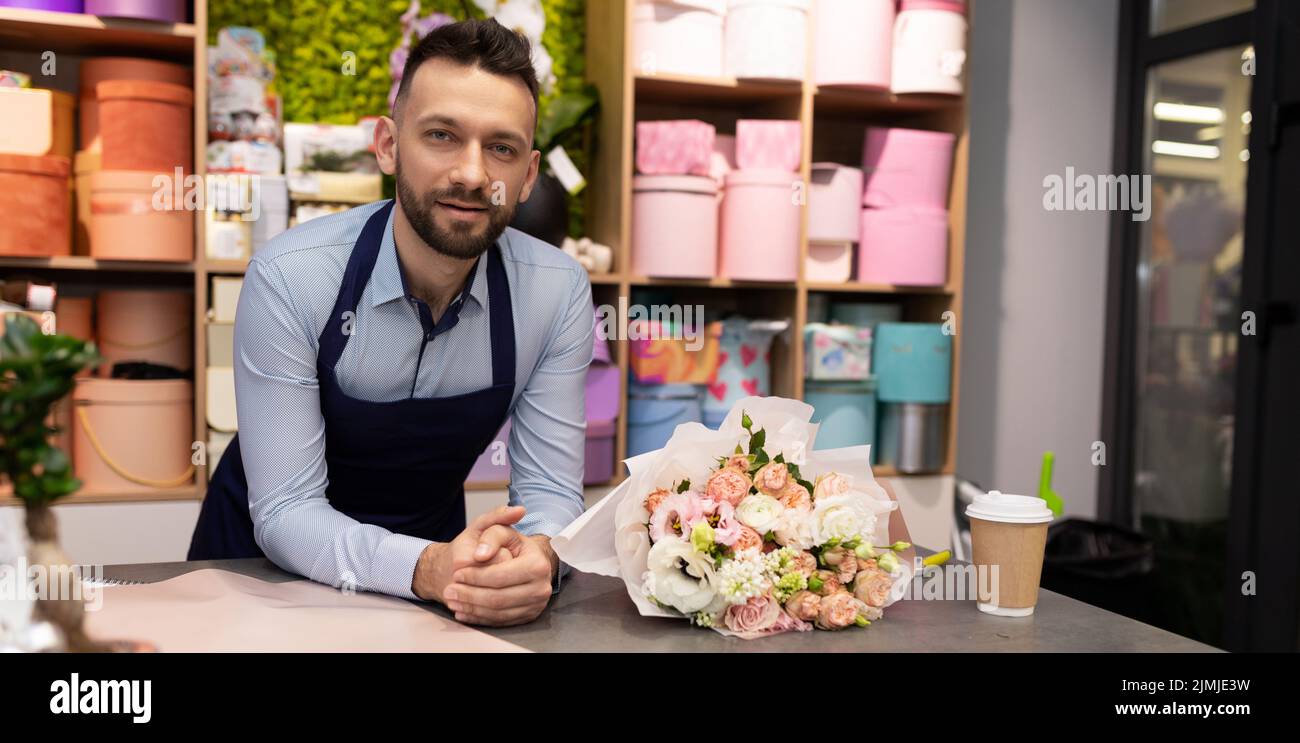 Charmanter Blumenhändler hinter der Theke eines Blumengeschäftes neben einem luxuriösen Blumenstrauß Stockfoto