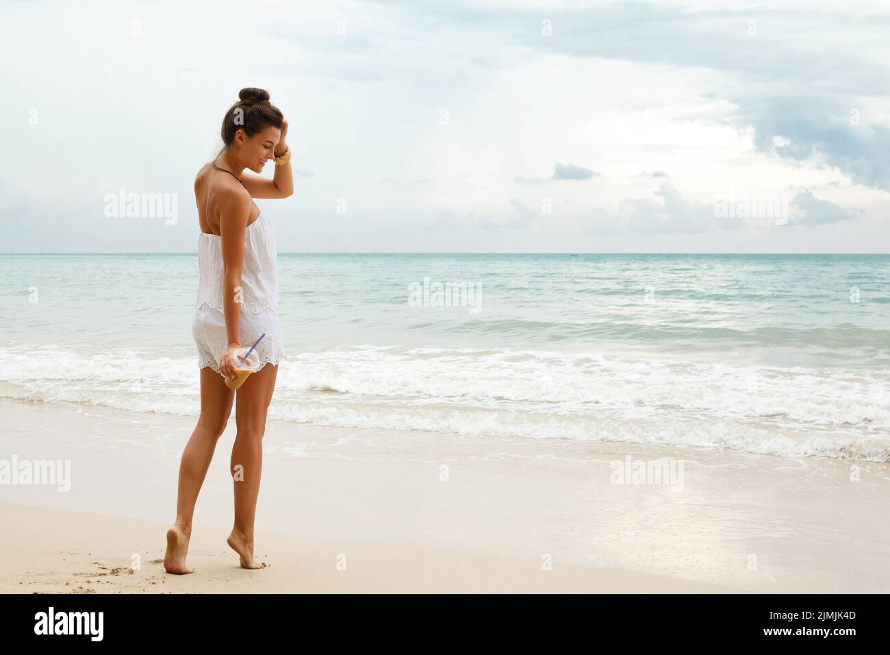 Schöne Frau trägt weißen Jumpsuit Spaziergang am Strand Stockfoto