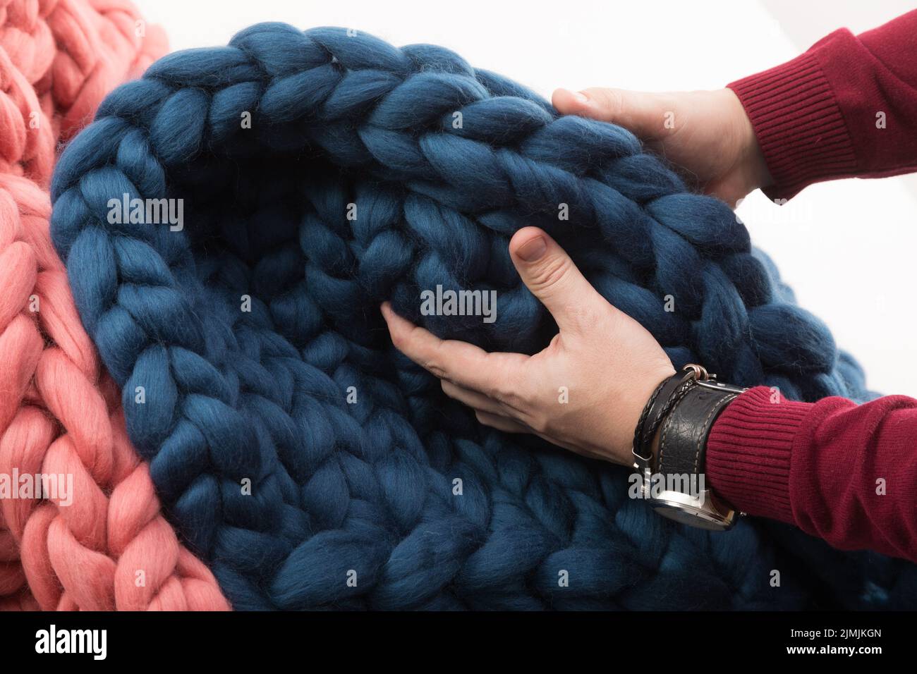 Herrenhände berühren eine grob gestrickte Decke aus Naturwolle Stockfoto