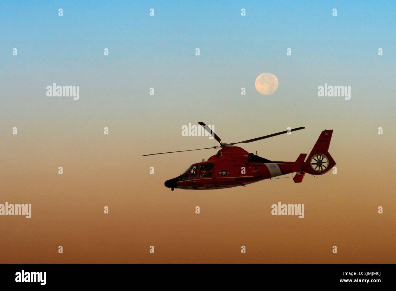 Ein Hubschrauber der US-Küstenwache fliegt in einem zusammengesetzten Bild an einem Vollmond vorbei. Stockfoto