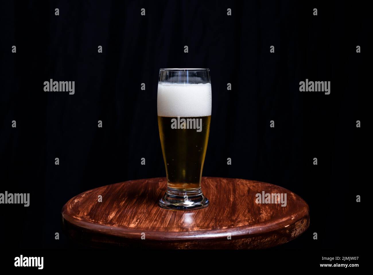 Studio Porträt eines Glasplatzes mit gelber Flüssigkeit, auf einer Holzbank, vor einem schwarzen Studiohintergrund. Salvador, Brasilien. Stockfoto