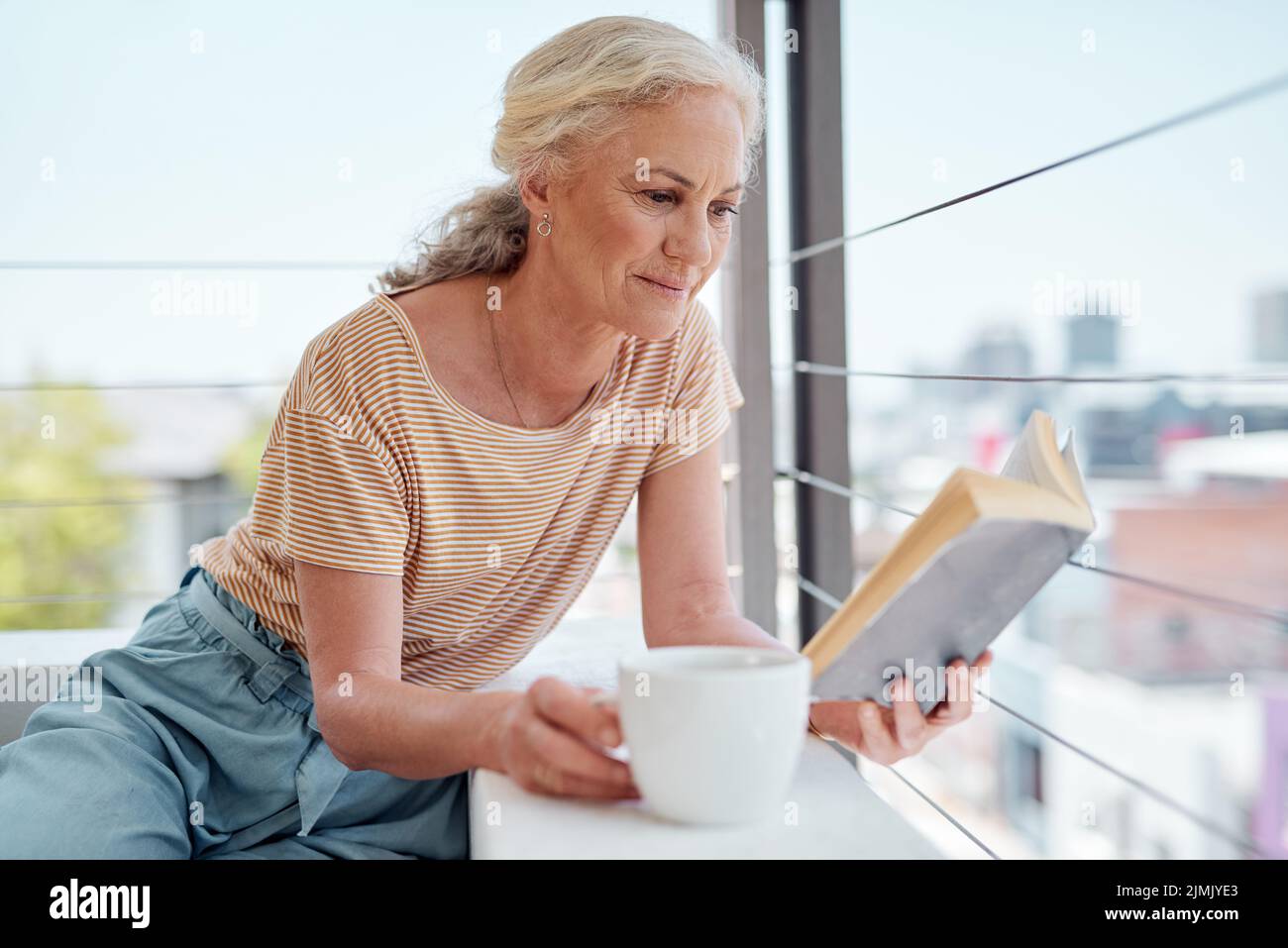Bücher sind eine Schatzkiste des Wissens. Eine reife Frau liest ein Buch und hat Kaffee auf ihrem Balkon zu Hause. Stockfoto