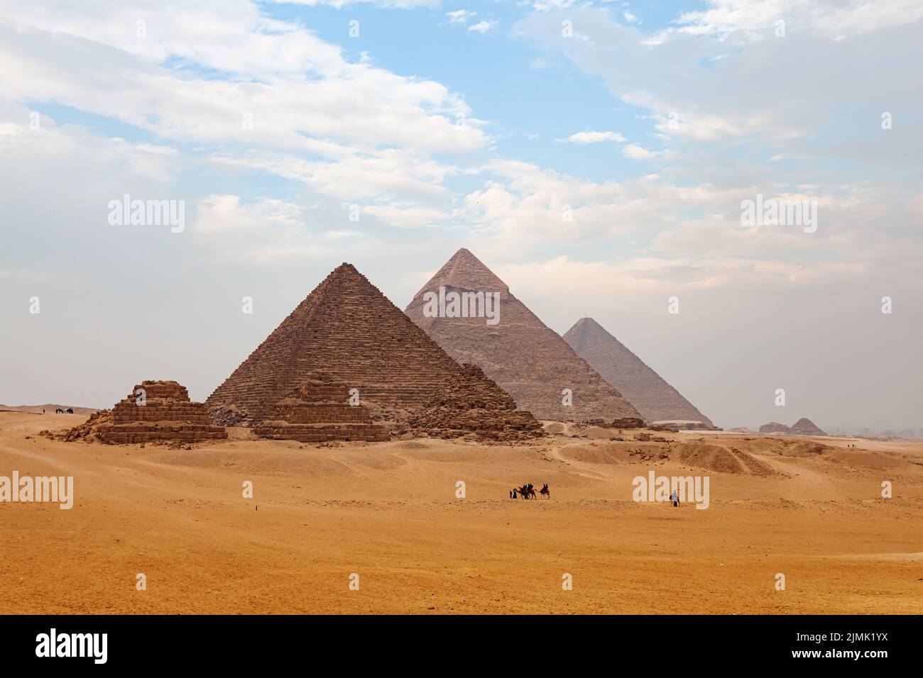 Blick auf das Gizeh Plateau mit Touristen und Einheimischen, die auf Kamelen reiten, und die große Pyramide im Hintergrund. Stockfoto