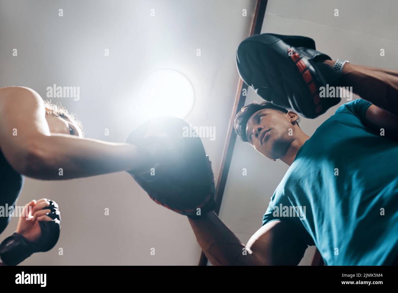 Jetzt ist der schwierige Teil... Aus dem niedrigen Winkel aufgenommen, in dem ein hübscher junger Fitnesslehrer eine Boxerin in einem Fitnessstudio trainiert. Stockfoto