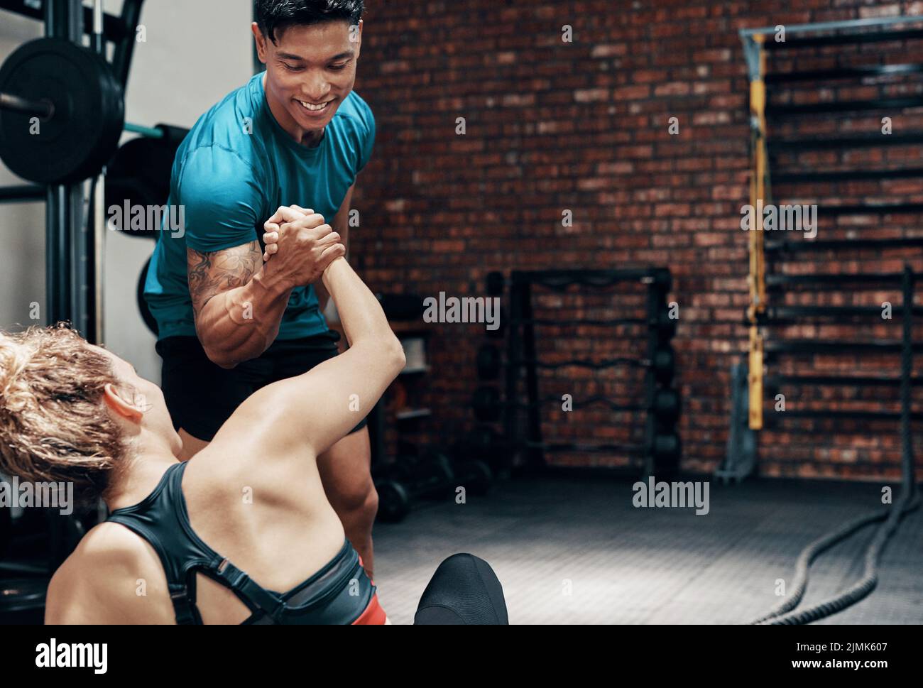 Ein hübscher junger Sportler, der seinem Partner im Fitnessstudio beim Aufstehen in einer Turnhalle hilft. Stockfoto