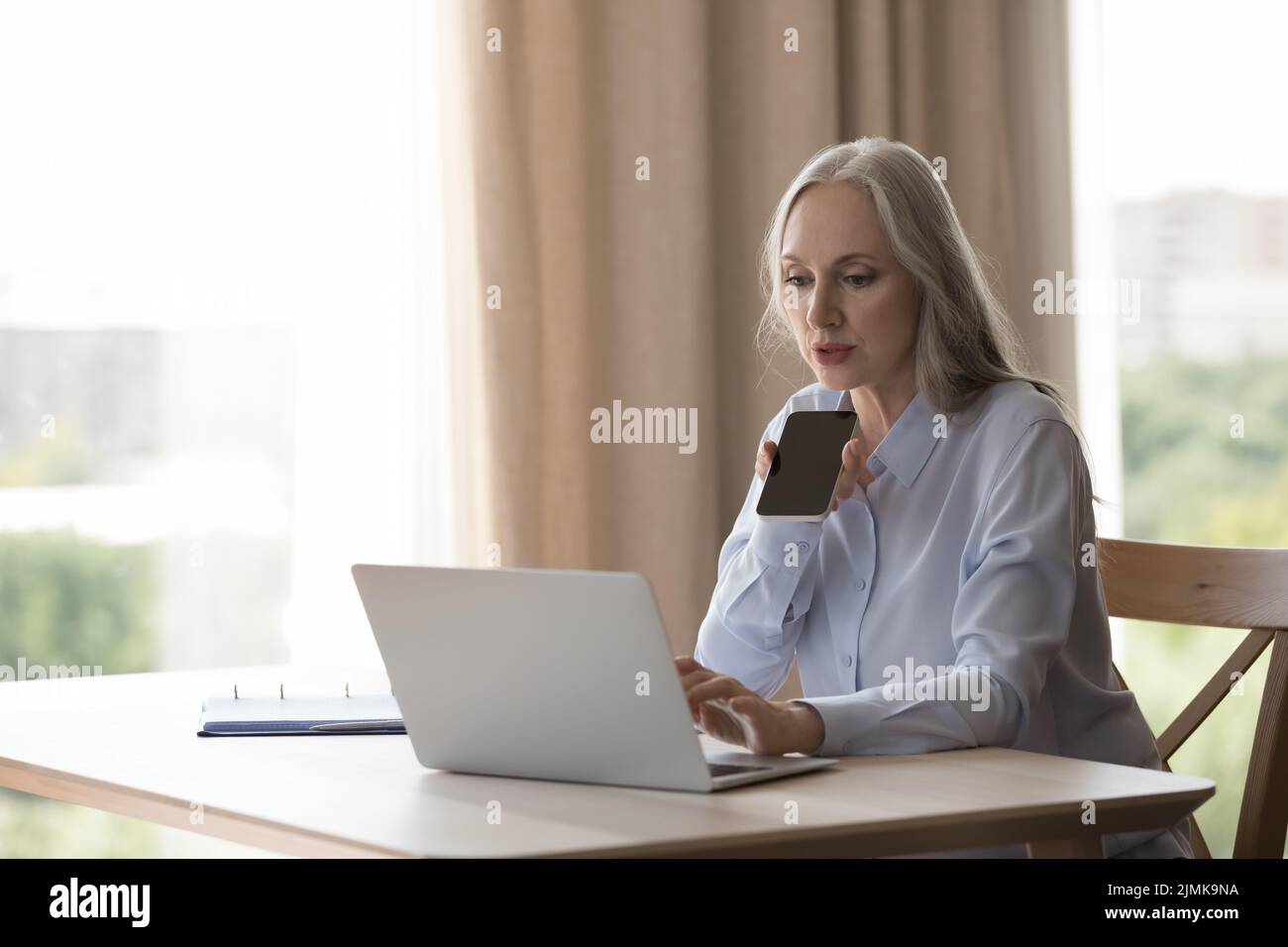Seriöse, konzentrierte ältere Geschäftsfrau, die eine Sprachnachricht aufzeichnet Stockfoto